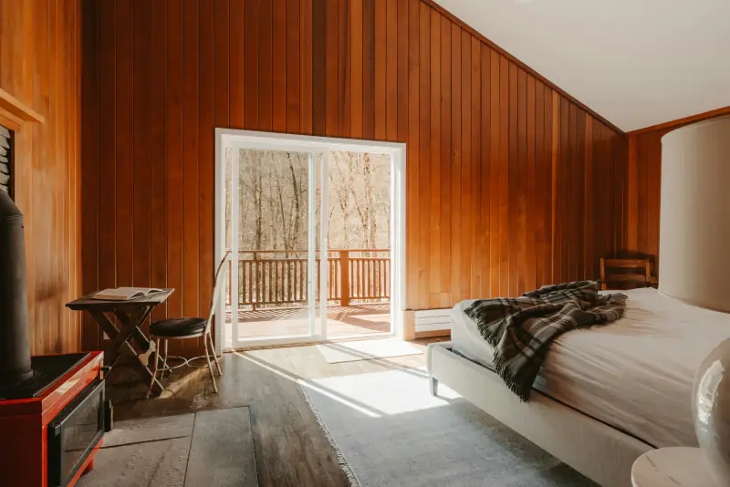 Zimmer mit Holzvertäfelung und Balkontür zum Wald in der ausgebauten Scheune