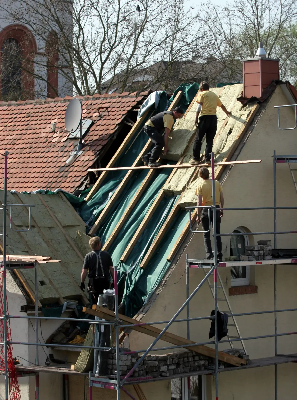 Zimmerer dämmen ein Altbaudach auf den Sparren, vom Gerüst aus